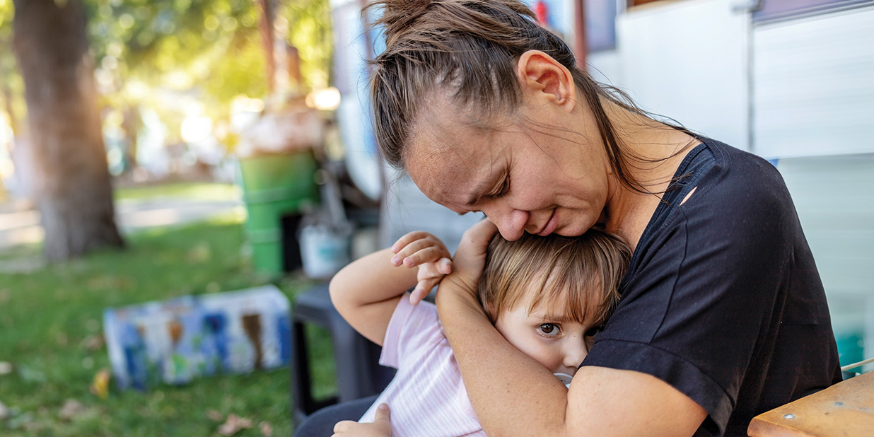 Stock image of a mother hugging her toddler outside a weatherboard house.
