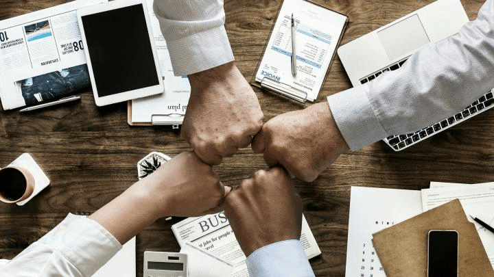 Group of business people reaching their hands across a paper-strewn table to form a group fist bump