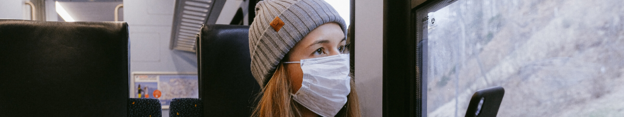 Woman wearing mask and winter hat on train with phone