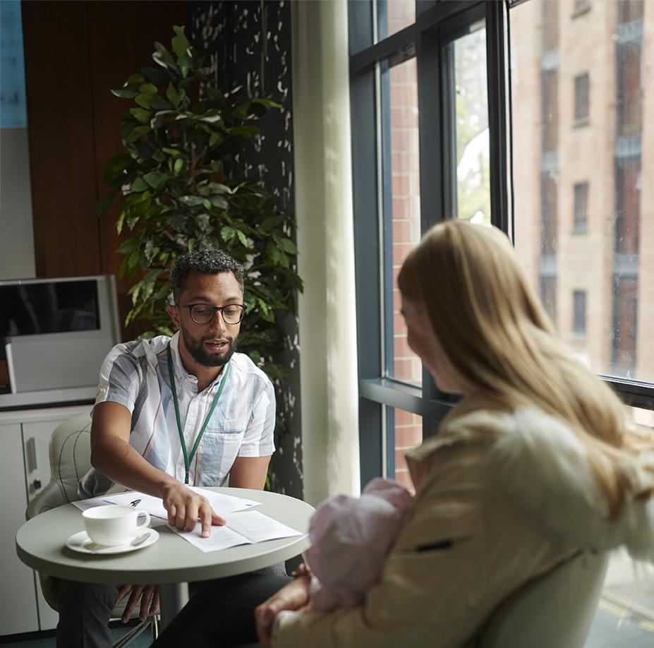 Two people sitting at a small table next to a window discussing documents while drinking coffee