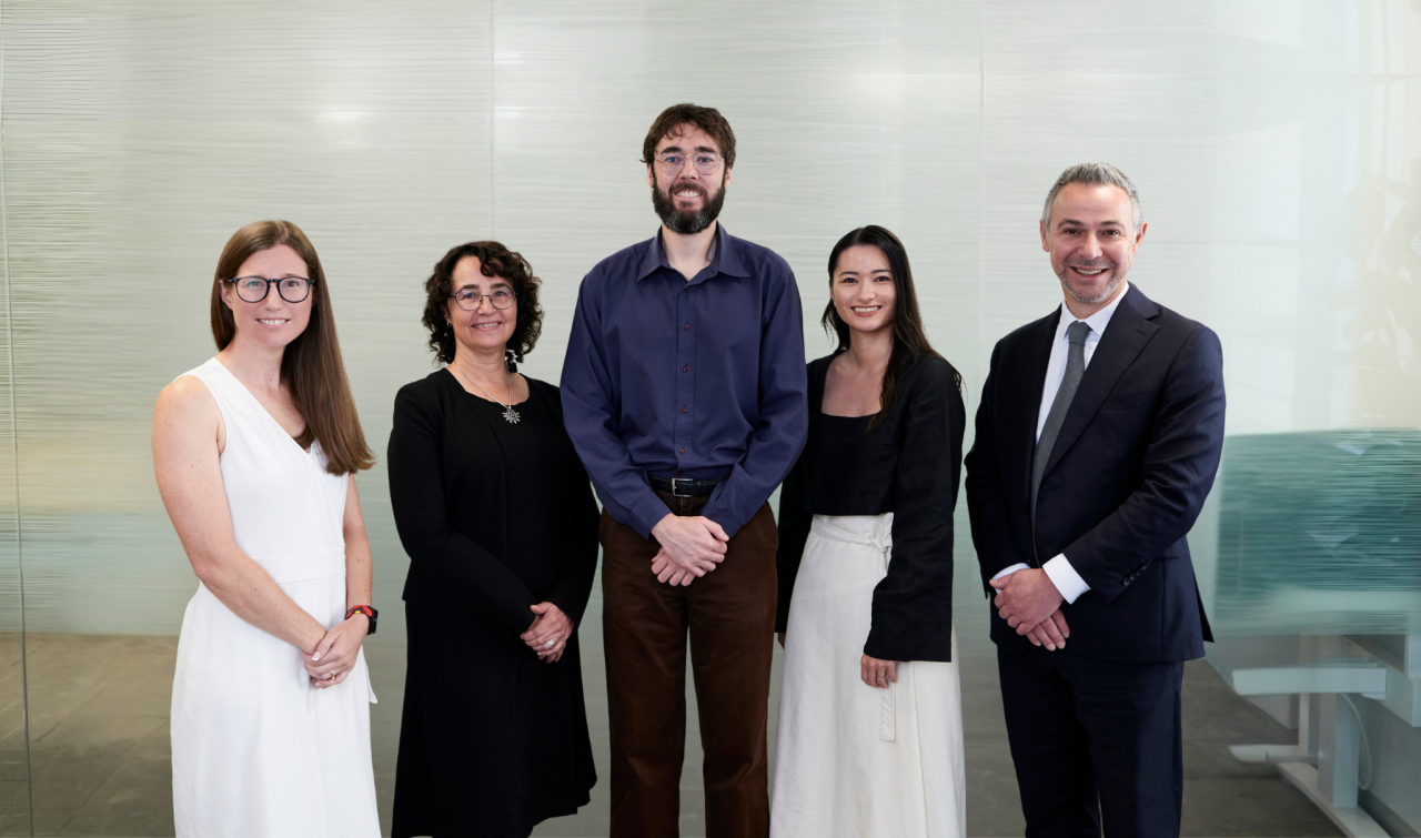 AHURI Professional Services team standing in AHURI office in front of frosted glass backdrop
