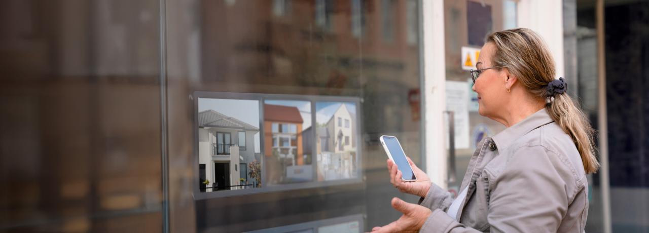 Person standing in front of real estate office looking in at available residences