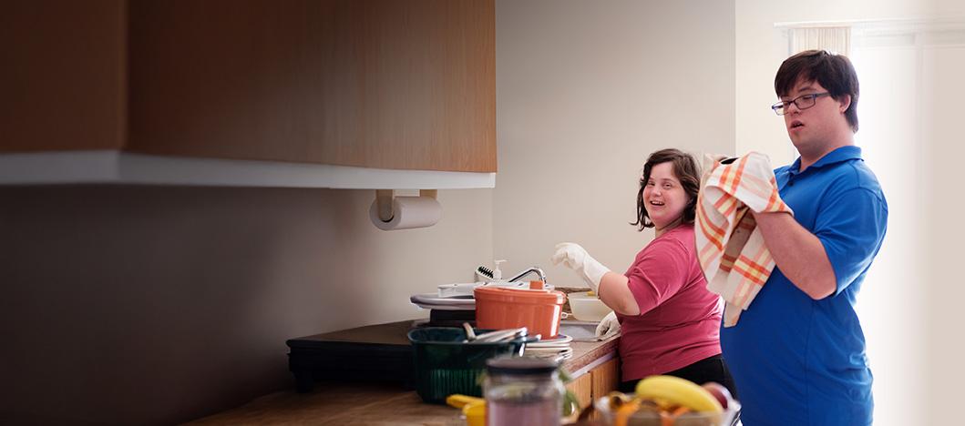 Two people with disability standing in kitchen together smiling toward camera
