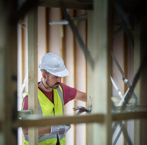 Man wearing hard hat and high vis vest, working on construction site for property being built