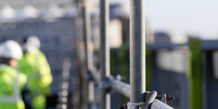 Focused image of scaffolding on construction site with two workers in hi-vis jackets in background