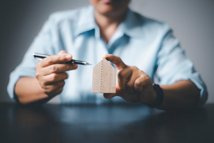 A person sitting at a desk holding a pen in one hand and a small wooden house in the other