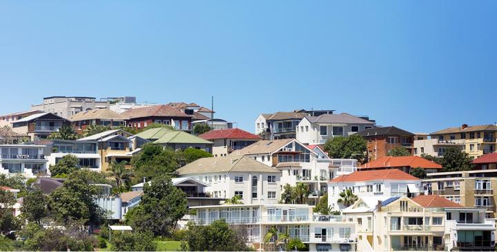 Aerial view of Australian suburb, with top half of image clear blue sky and bottom half a stack of houses on an incline