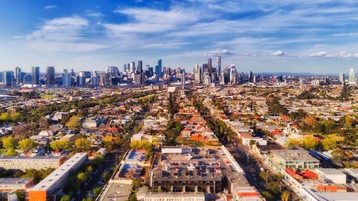 Aerial view of Melbourne city CBD high-rise towers from Port Melbourne and Southbank above residential suburb house roofs and local streets, roads, cars and parks.