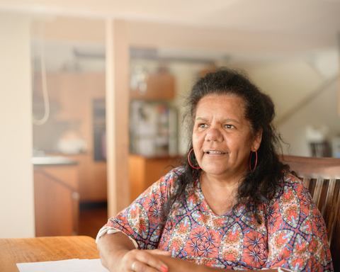 First Nations woman sitting at table in a house, smiling ahead