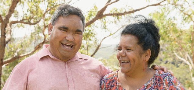 Two First Nations individuals smiling outside with trees in background