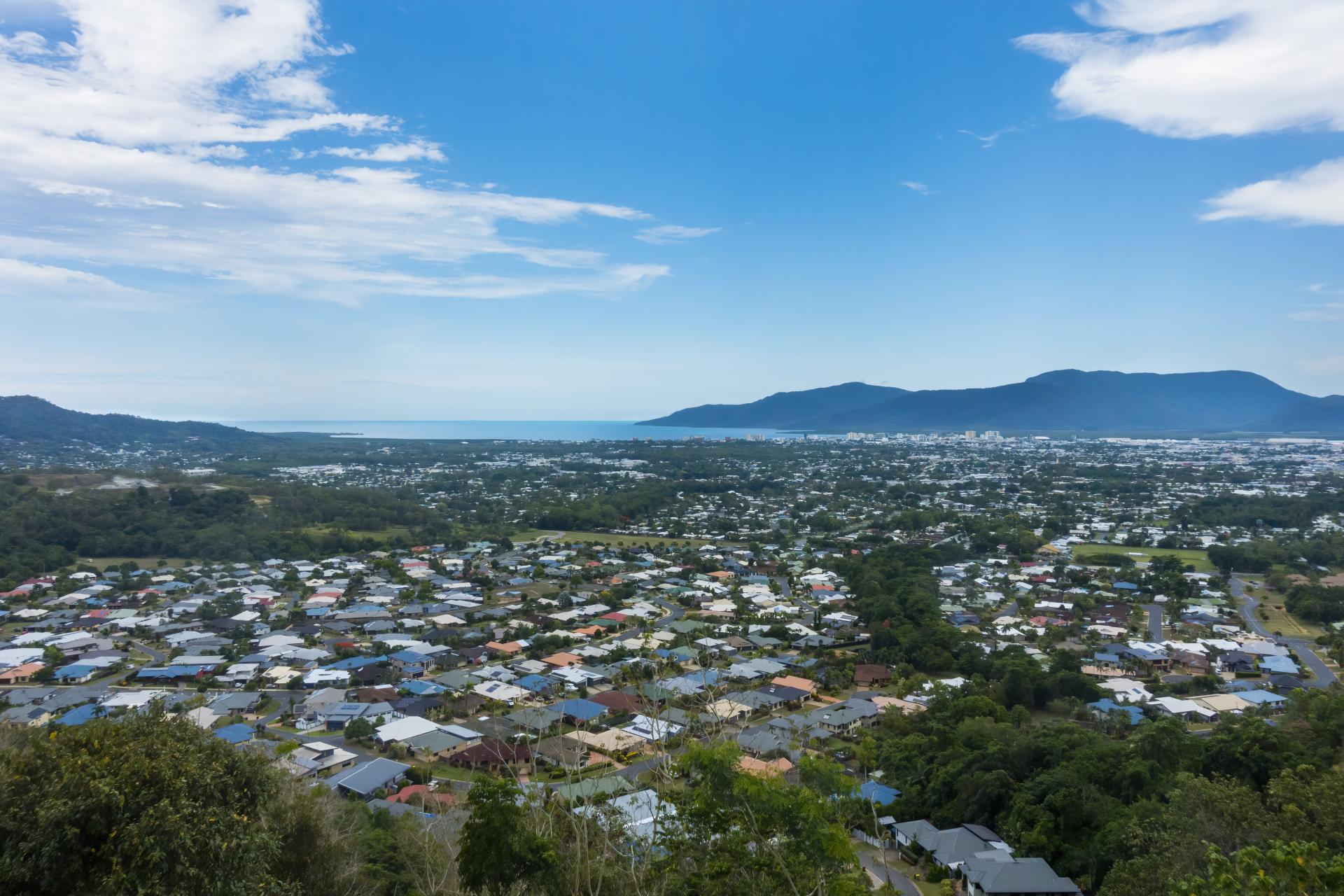 Wide aerial view of Cairns city featuring suburbs surrounding by lush greenery and a mountain range and water in the distance