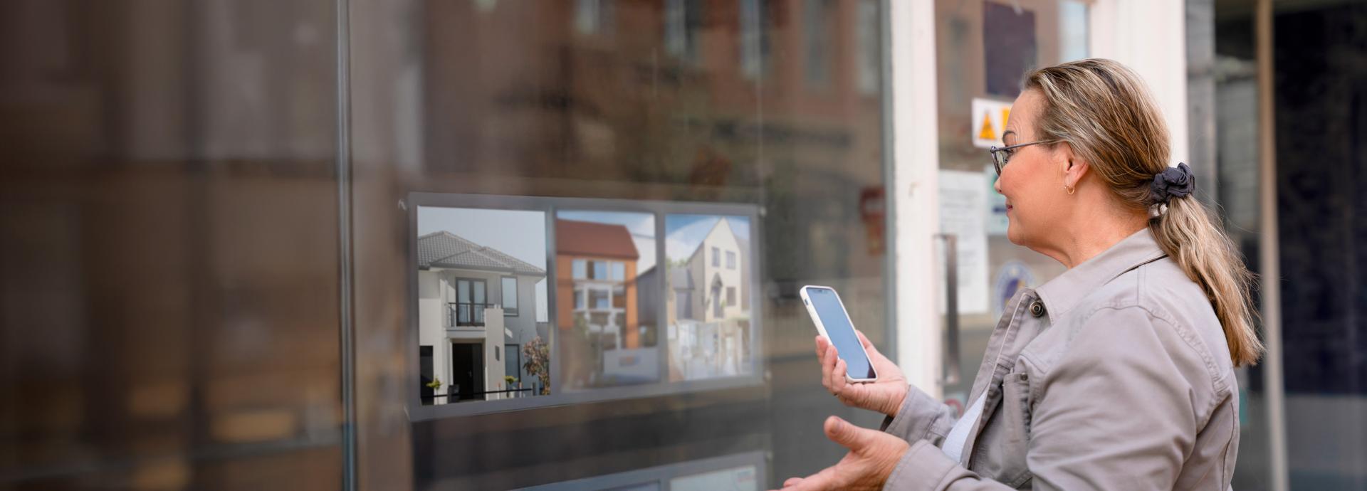 Person standing in front of real estate office looking in at available residences