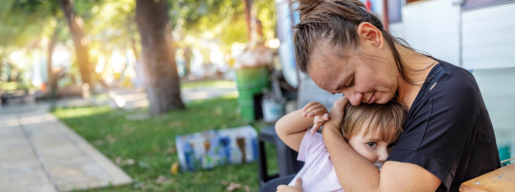 Stock image of a mother hugging her toddler as they sit outside a house.